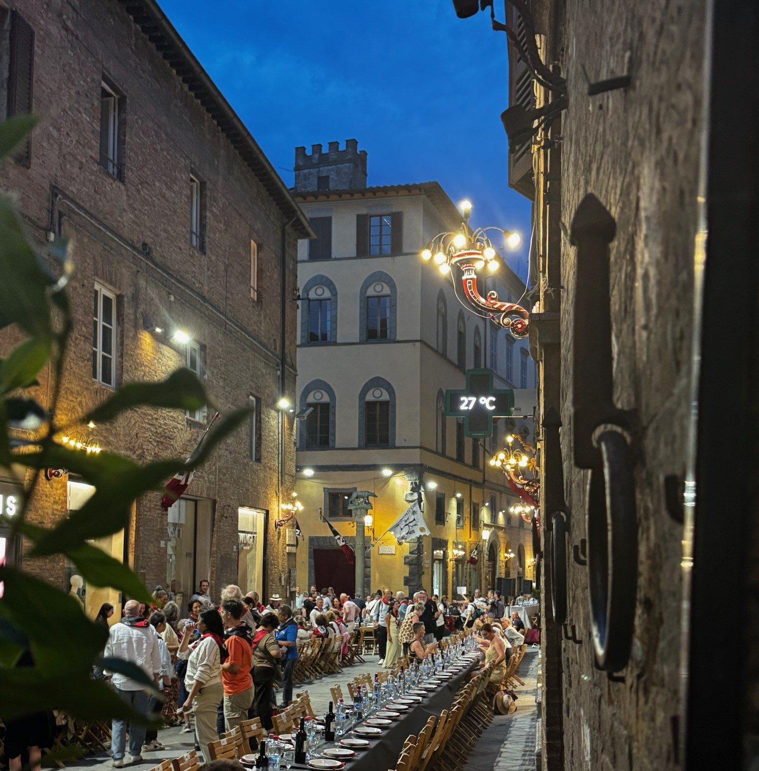 Long dinner tables set down a Siena street at dusk during a contrada dinner