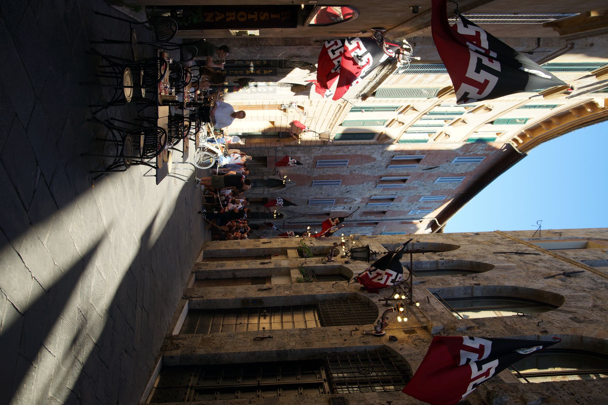 Café tables under contrada flags in a Siena street