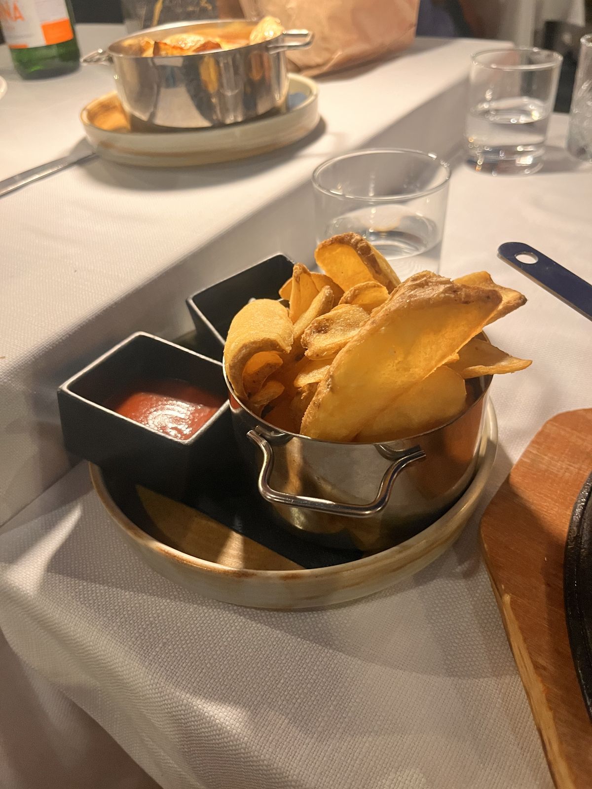 Hand-cut chips in a steel pail with ketchup at Il Tufo, a pan of roast potatoes behind