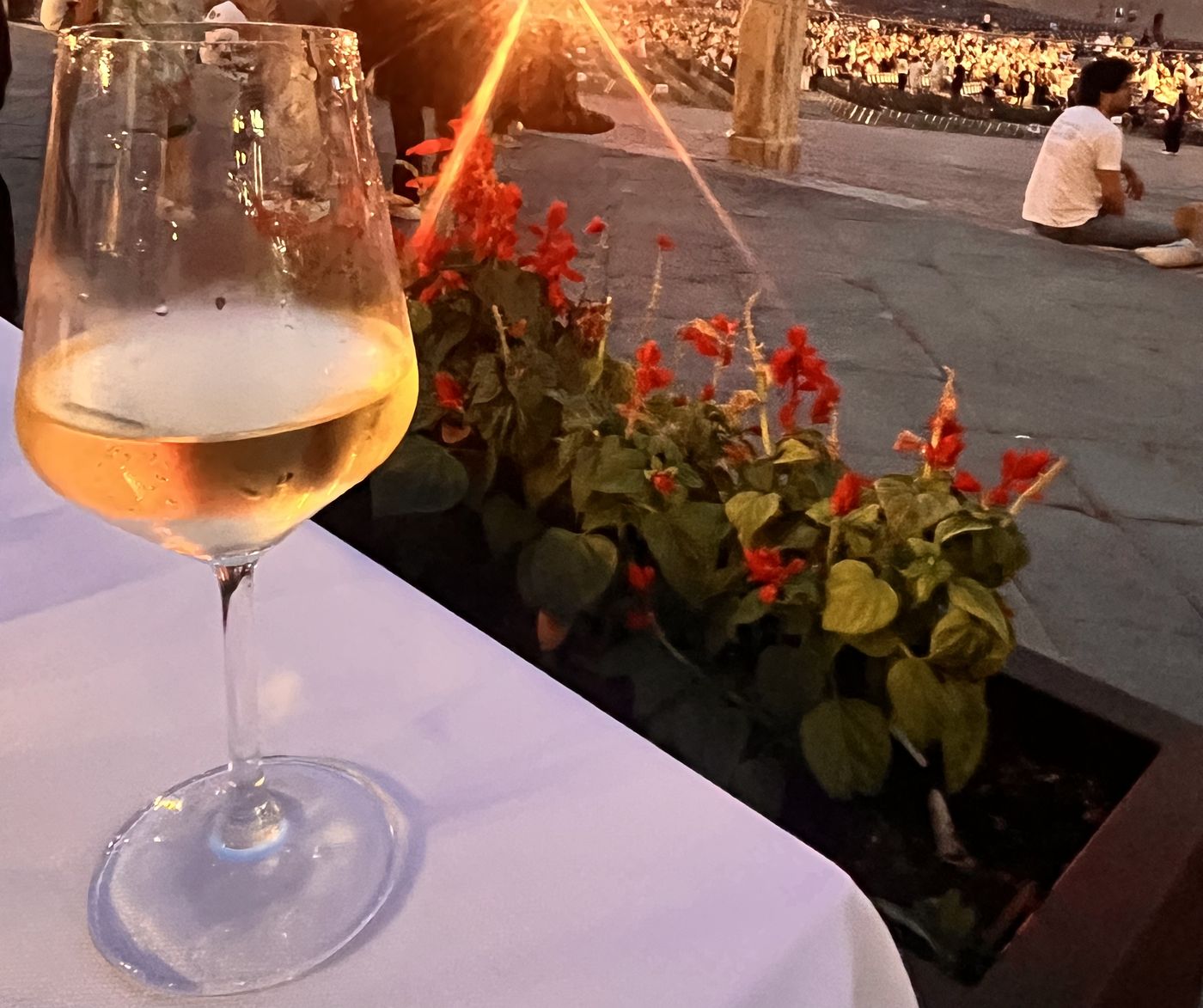 Glass of white wine on a linen-set terrace table at Il Tufo, with the Piazza del Campo concert crowd at dusk