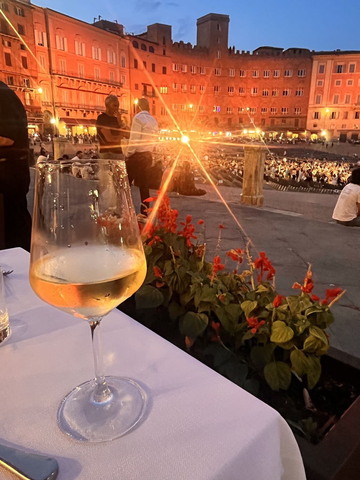 Aperitivo hour above Piazza del Campo — a glass of white wine at a terrace table as a summer concert crowd gathers below